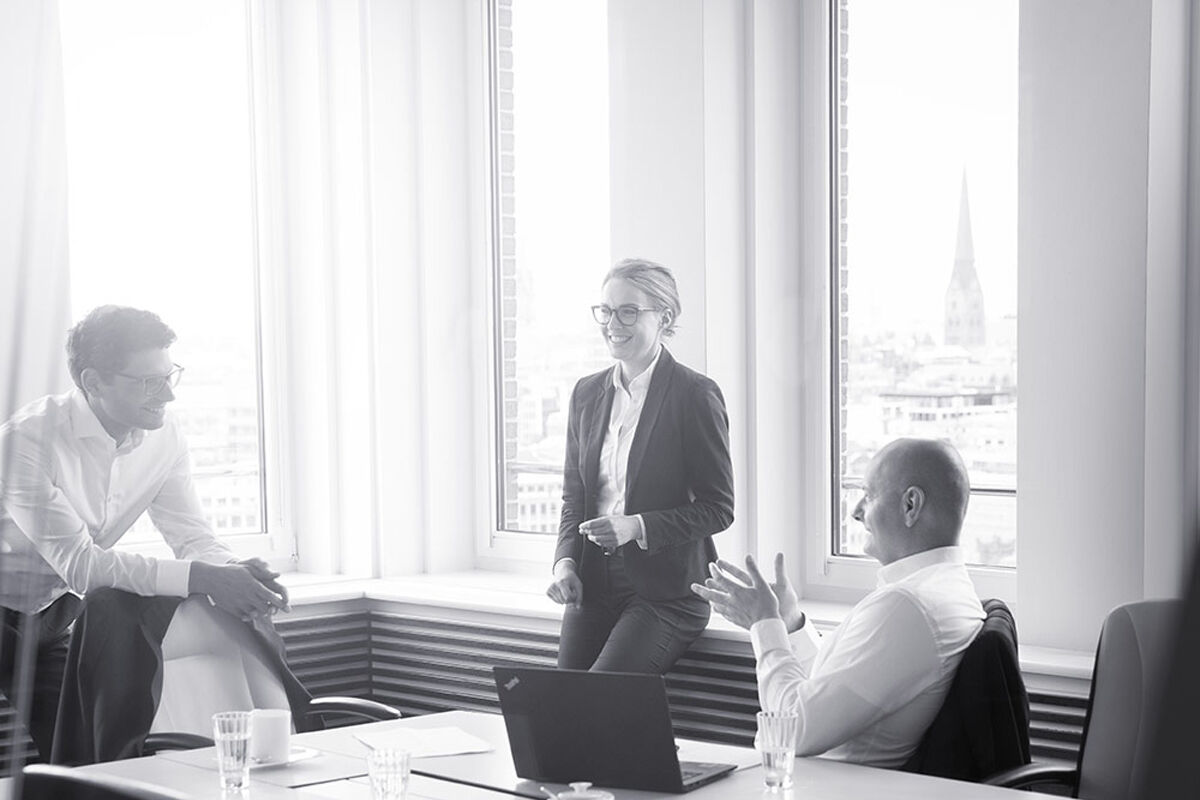 Drei Personen in Anzügen unterhalten sich in einem Konferenzraum.