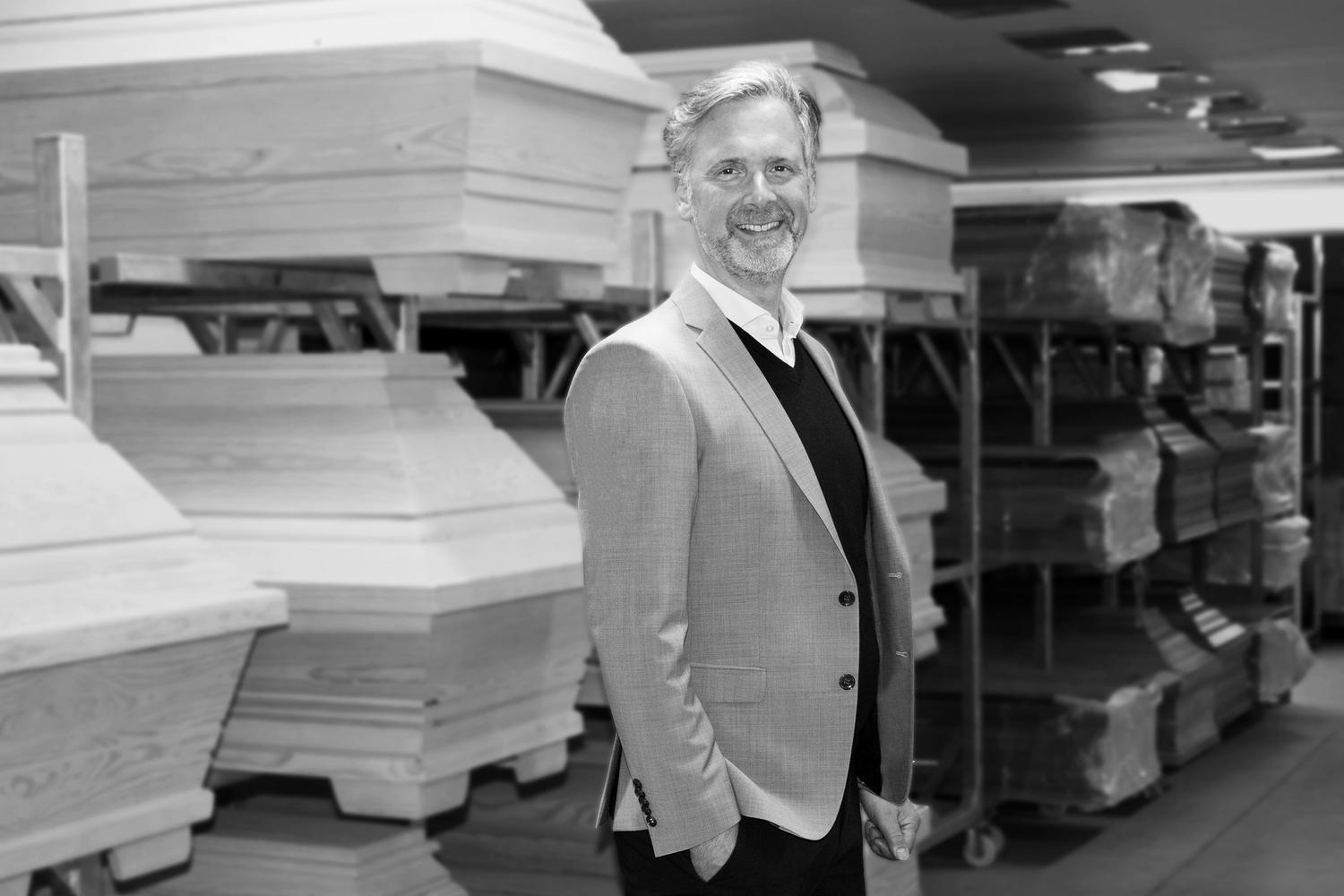 CMO Dirk Haase steht in einem Sakko gekleidet vor mehreren aufgereihten Holzsärgen.