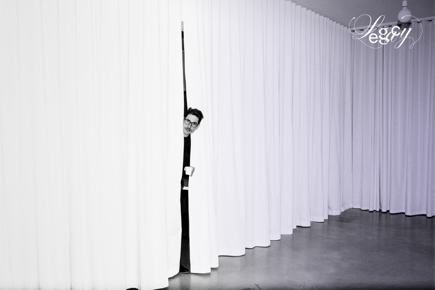 Raum mit weißem Vorhang an den Seiten, durch den Jan mit einer Kaffetasse in der Hand hervorschaut