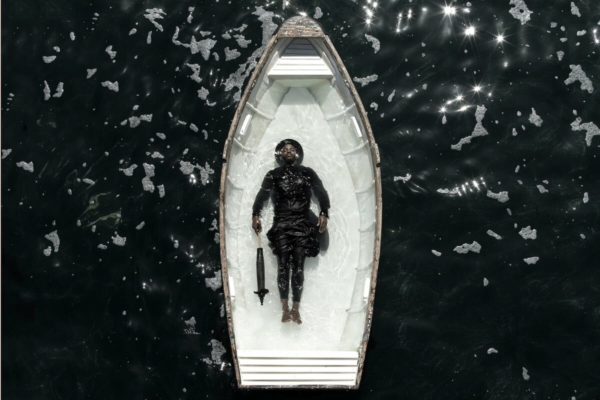 Rowing boat filled with water with woman lying in the middle of the ocean