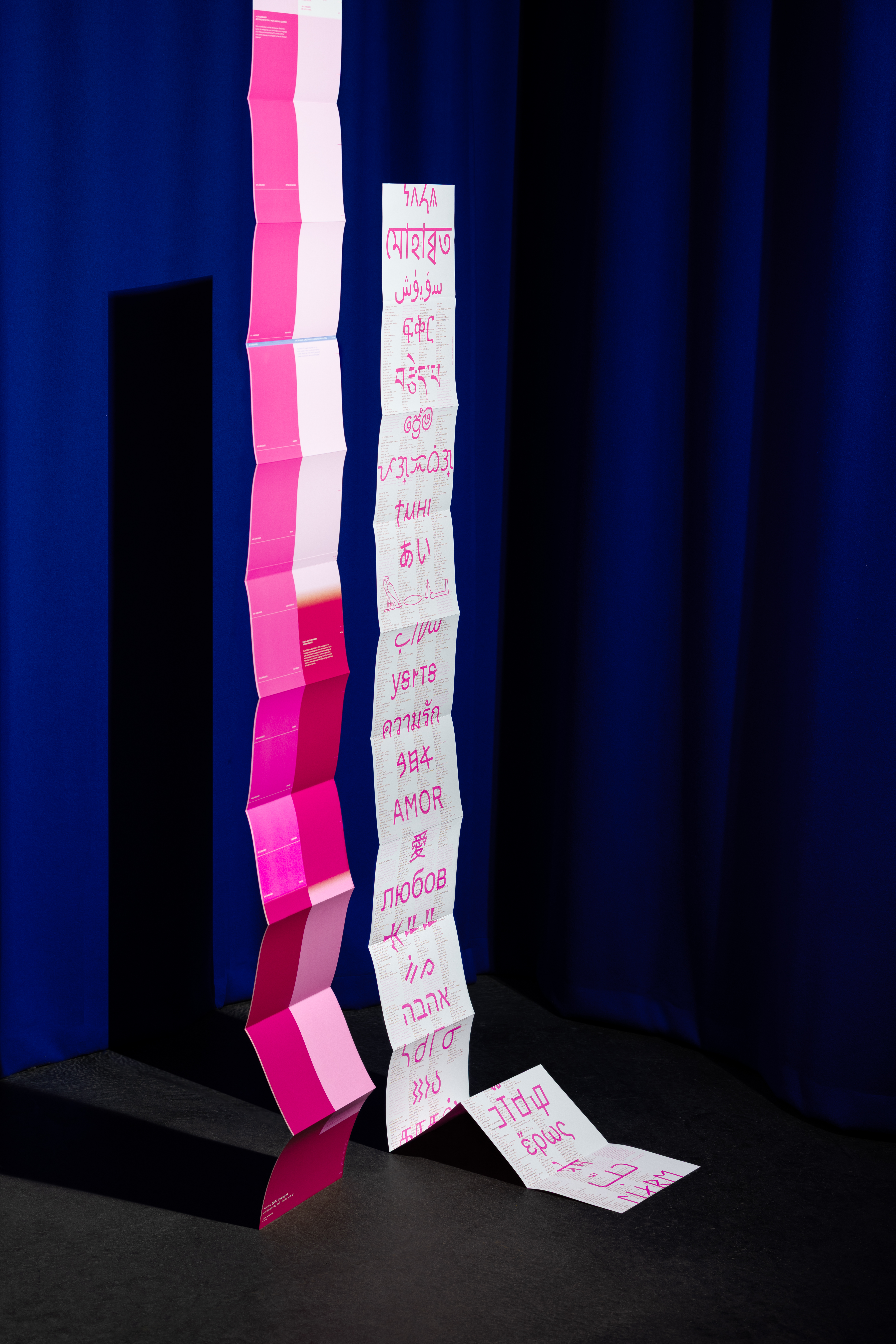 Zwei lange Leporellos hängen auseinandergefaltet in einem dunklen Raum.